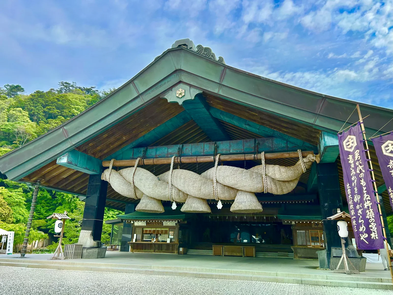 出雲大社神樂殿屋簷下掛著大型注連繩，兩側有紫色旗幟