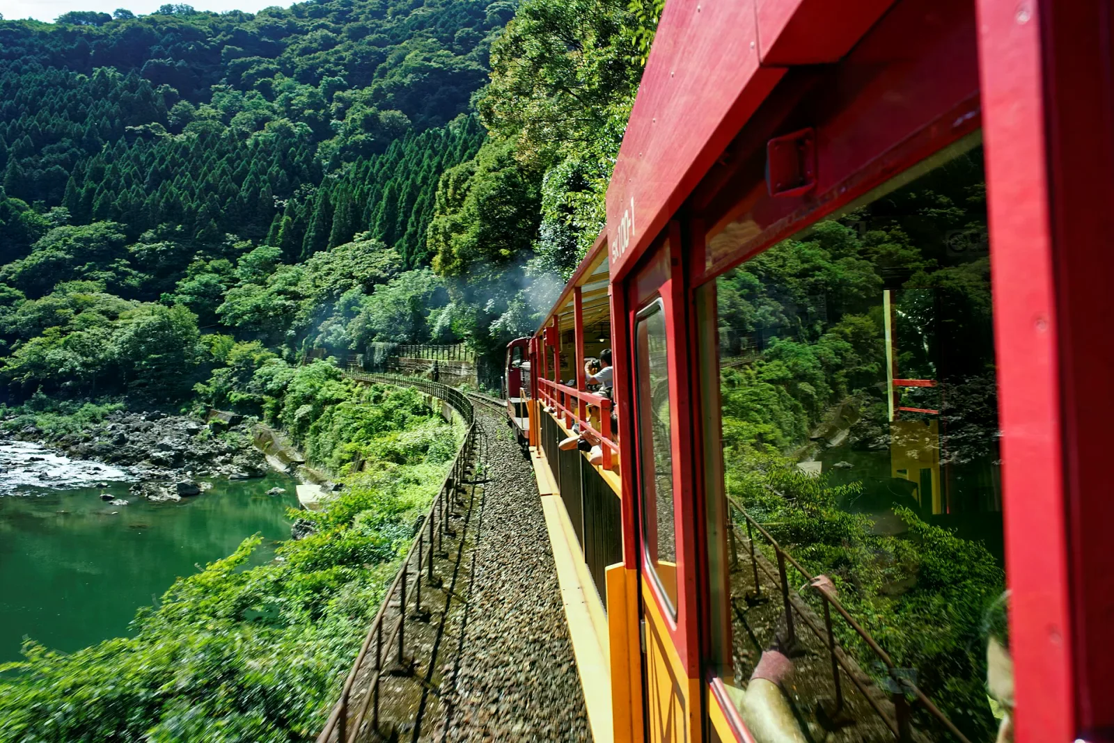 紅色開放式車廂沿保津川峽谷行駛，兩旁是翠綠河岸