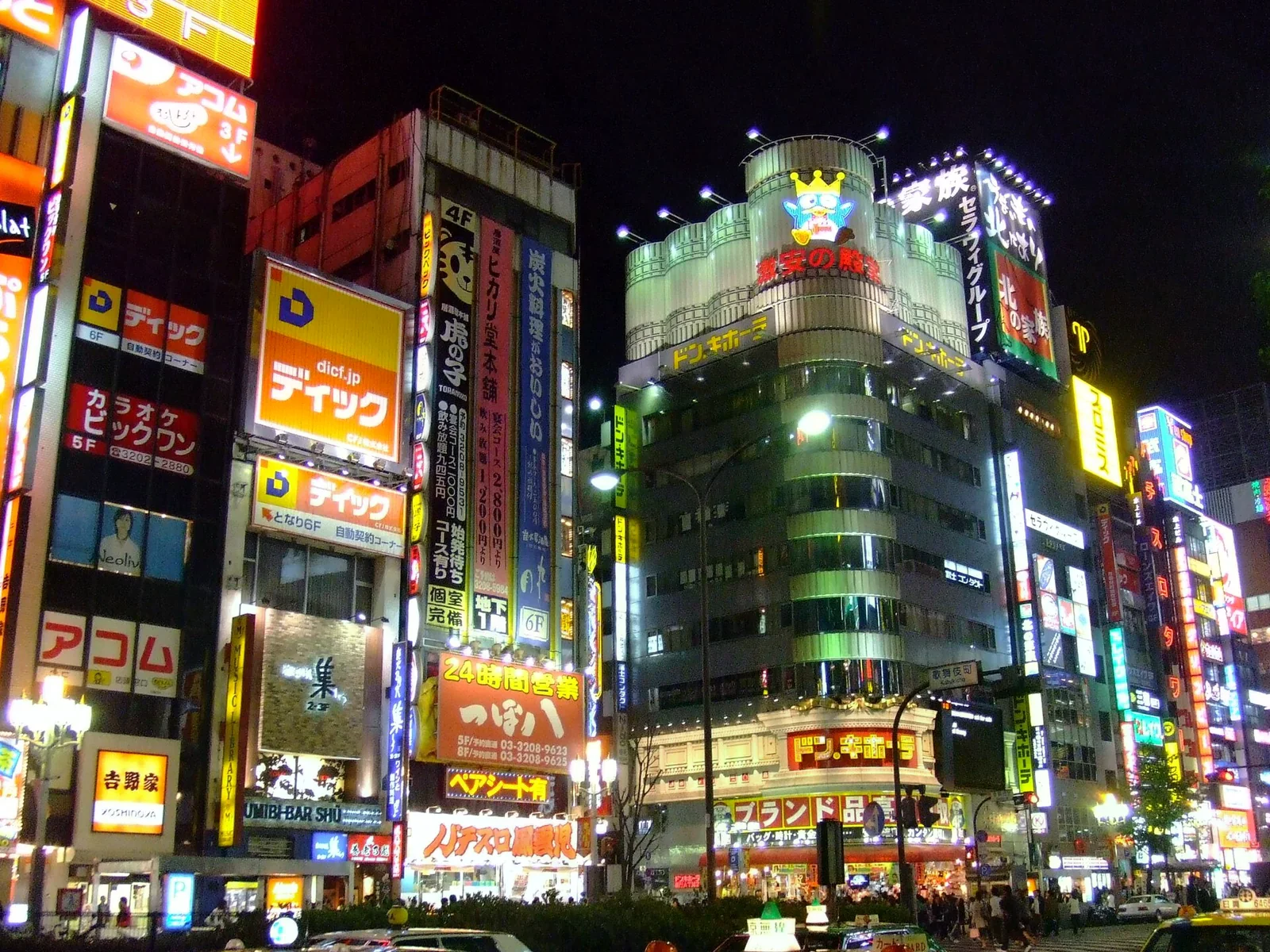 夜晚的新宿商業區，兩側大樓掛滿霓虹招牌，右側可見唐吉訶德的招牌建築